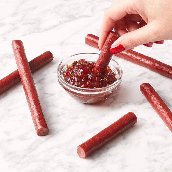 Several Barbeque Beef Snack Sticks being dipped in a bowl of sauce