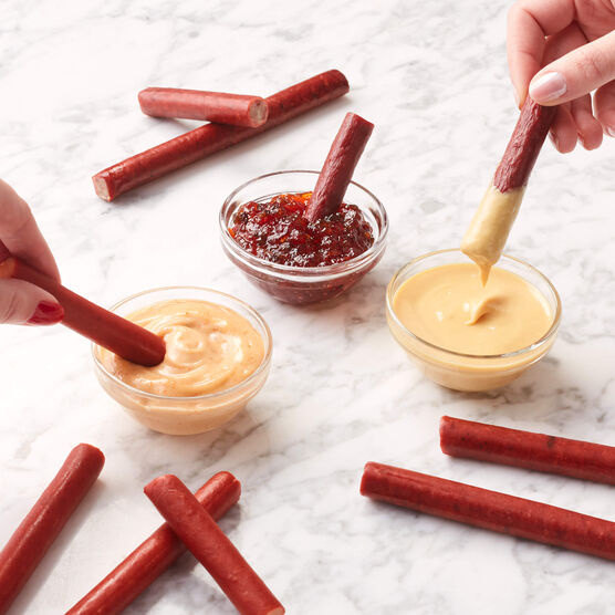 Various beef and chicken snack sticks being dipped in sauces on marble background