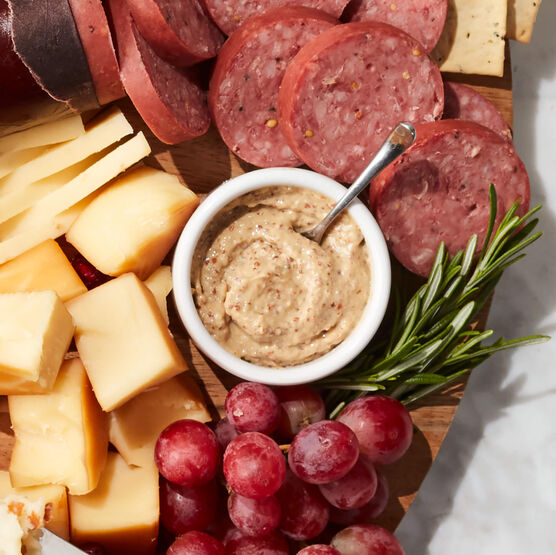 Belgian Ale Mustard in small bowl on charcuterie board with summer sausage and cheese
