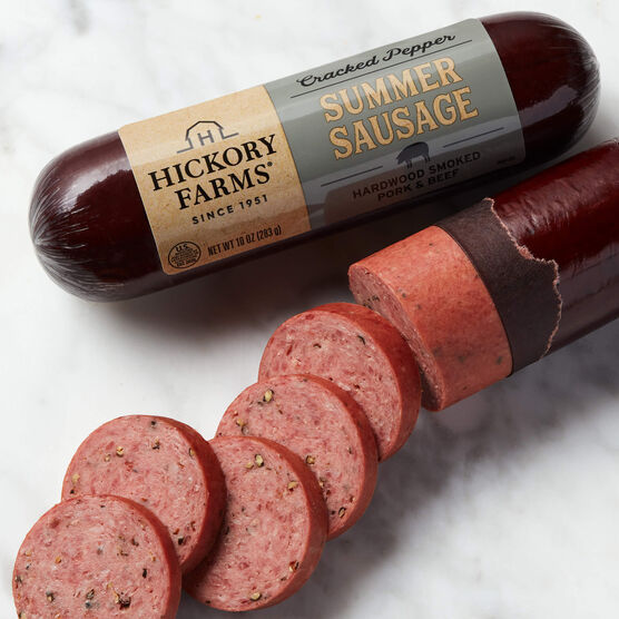 Two Cracked Pepper Summer Sausages, one sliced and one in packaging on marble background