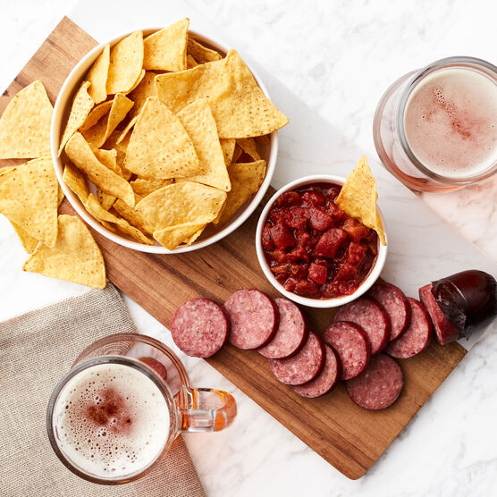 Chips and Salsa with cut up summer sausage on cutting board