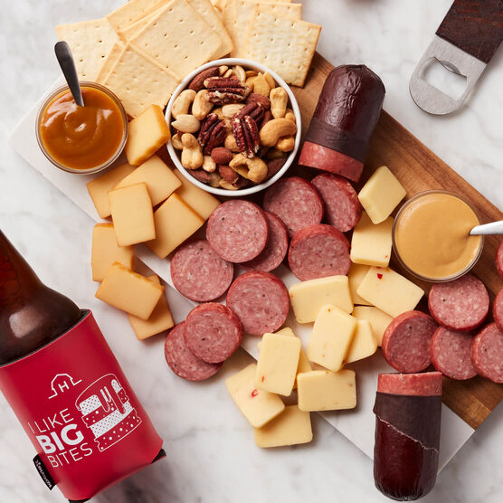 Charcuterie display of savory snack gift with Farmhouse summer sausage, cheddar cheeses, mustards, mixed nuts, crackers, bottle opener, and reusable koozie.