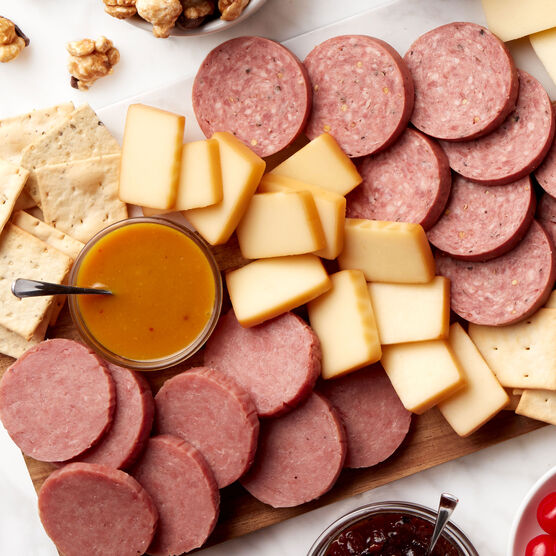 Alternate view of Hickory Farms honey pineapple mustard on a charcuterie board with turkey summer sausage, beef summer sausage, and smoked cheddar