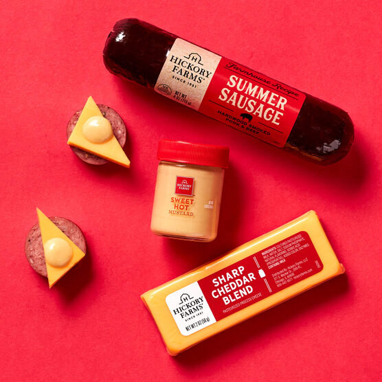 Classic Meat and Cheese Stocking Stuffer components, summer sausage, mustard, and cheese on red background