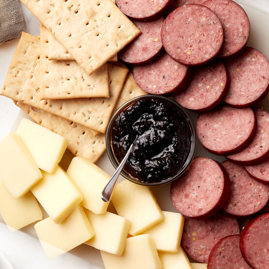 Alternate view of Hickory Farms hot pepper bacon jam on a charcuterie board with beef summer sausage, cheese, and flatbread crackers