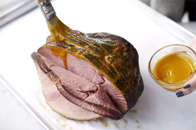 A spiral sliced ham being brushed with Honey and Pineapple mustard