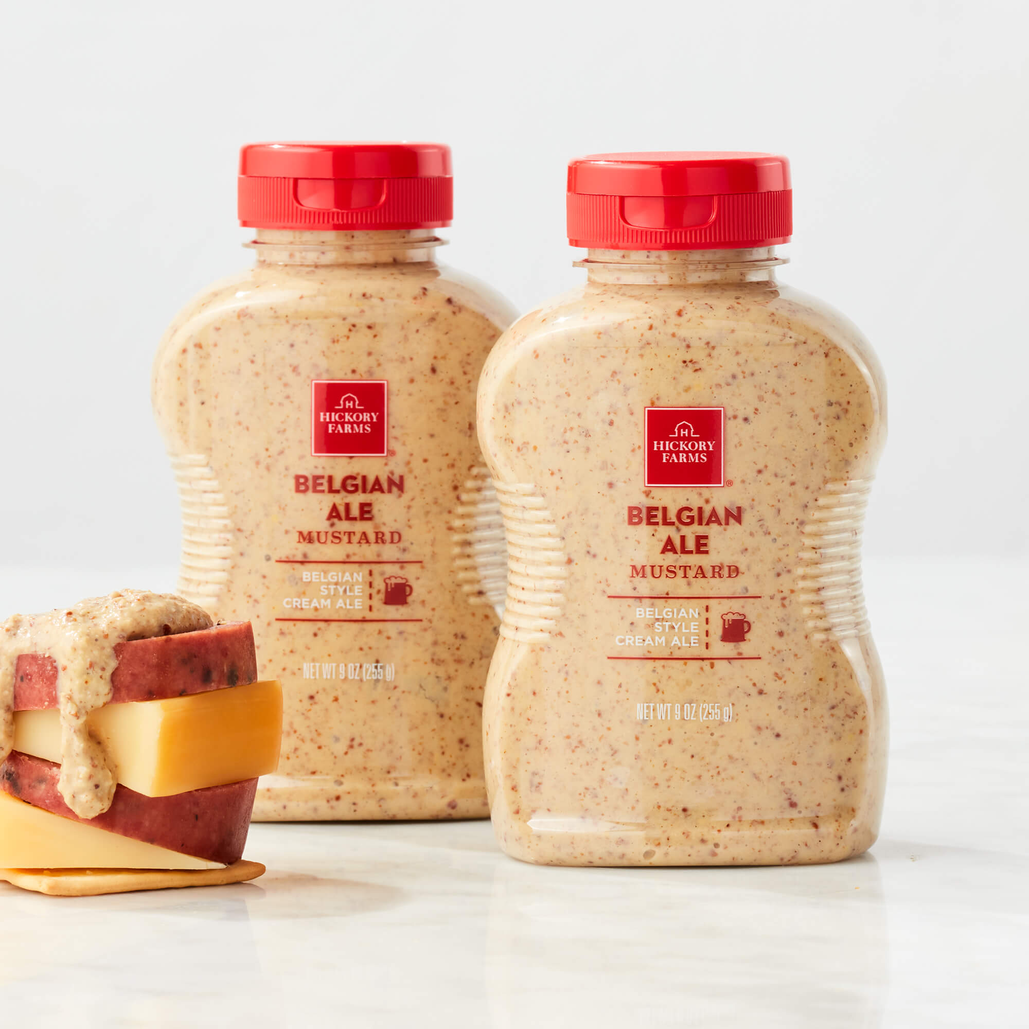 Hickory Farms Belgian Ale Mustard squeezers on marble background with stack of meat and cheese on cracker